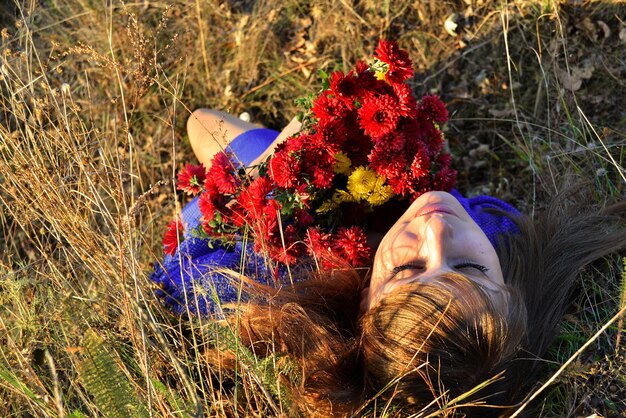 Une femme allongée dans l'herbe avec un bouquet de fleurs à la main.