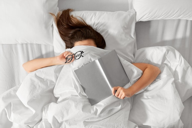 Une femme allongée dans un lit avec un livre et des lunettes.