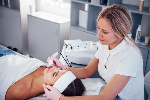 Femme allongée dans un salon de spa et ayant une procédure de nettoyage du visage par un cosmétologue professionnel.