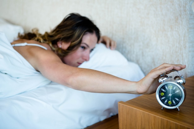 femme allongée dans son lit, tendant la main pour éteindre son réveil