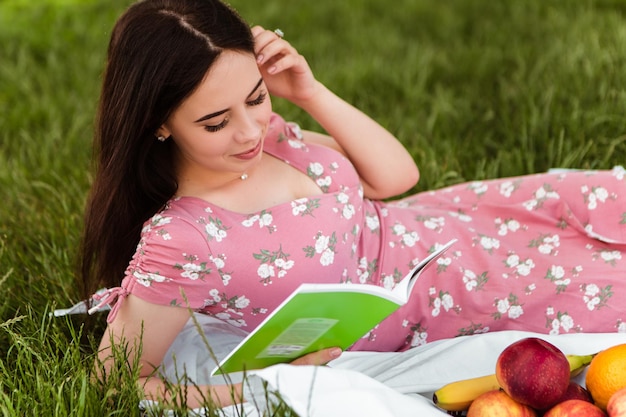 Femme allongée sur un drap blanc, lisant un livre, souriant