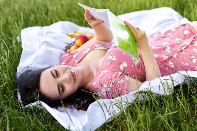 Femme allongée sur un drap blanc tenir et lire des notes de livre Dame se reposer dans le parc de la ville