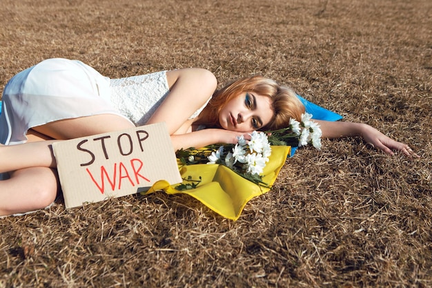 Femme allongée sur le drapeau ukrainien avec signe de protestation Stand with Ukraine concept