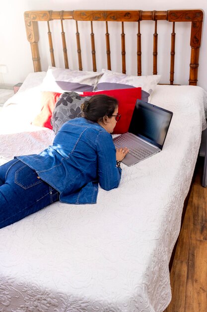 Femme allongée sur le lit à l'aide d'un ordinateur portable et dans une chambre confortable le matin