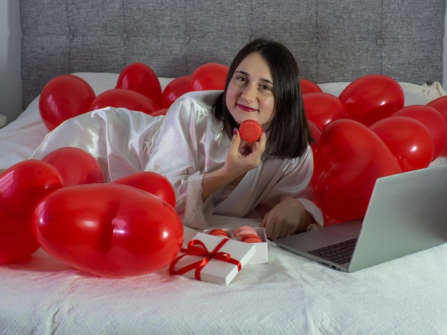 Femme allongée sur le lit avec des ballons rouges pour la fête de la Saint-Valentin