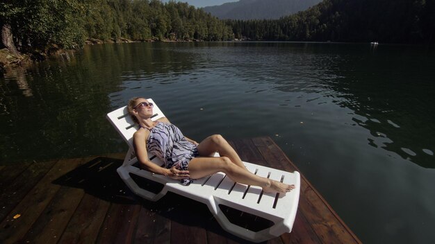 Femme allongée sur un lit de bronzage avec des lunettes de soleil et un châle en soie bohème Une fille se repose sur une jetée sous-marine en bois d'inondation Le trottoir est recouvert d'eau dans le lac