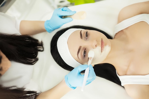 Femme allongée sur une table de massage dans un spa de santé pendant qu'un masque facial est appliqué sur son visage