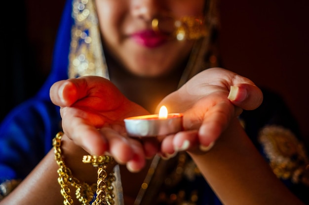 Femme allumant des diyas avec un piercing au nez nuth nath et le teck doré avec un sari de mode traditionnel