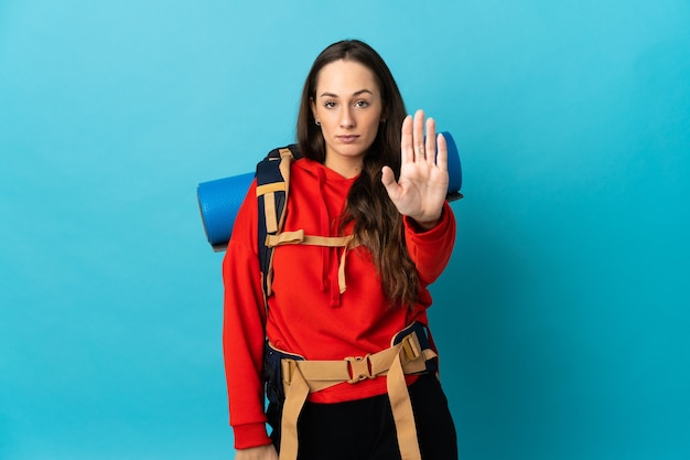 Femme d'alpiniste avec un gros sac à dos sur fond isolé faisant un geste d'arrêt