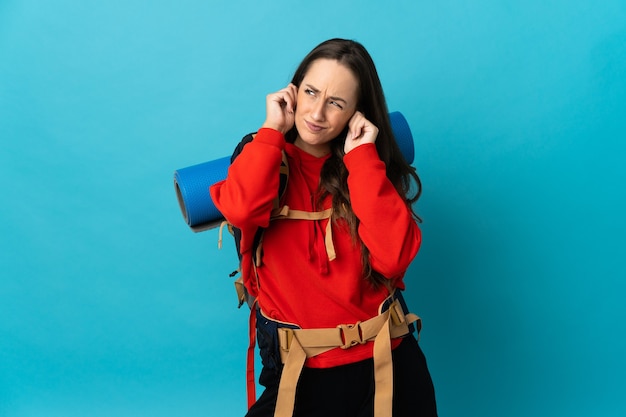 Femme d'alpiniste avec un gros sac à dos sur fond isolé frustré et couvrant les oreilles