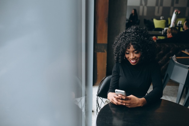 Femme américaine afro avec téléphone au café