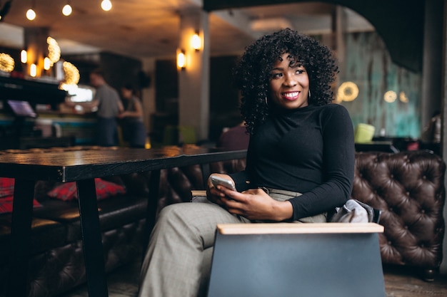 Femme américaine afro avec téléphone au café