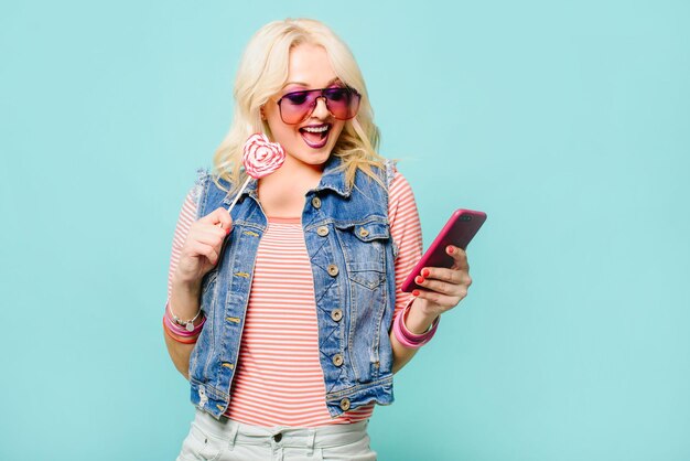 Femme américaine blonde avec émotion positive à l'aide de smartphone sur fond de couleur