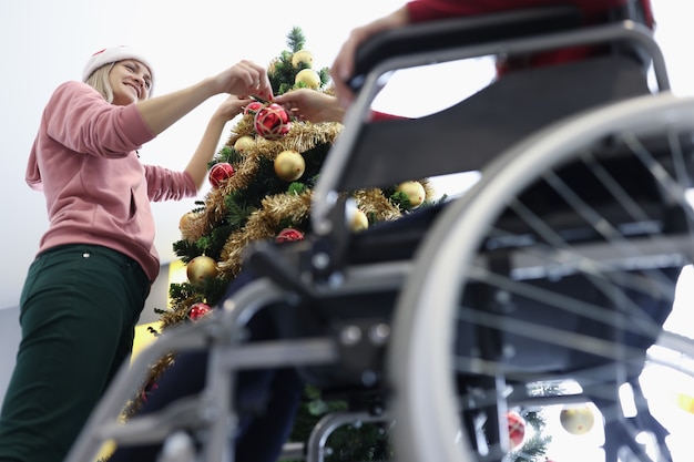 Femme et ami en fauteuil roulant suspendu boule de Noël rouge sur l'arbre du nouvel an. Se préparer à célébrer Noël au concept de centre de réadaptation