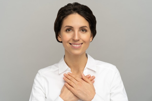 Femme amicale tient les mains sur la poitrine, se sent reconnaissante pour l'amour, l'appréciation, la reconnaissance et le soutien