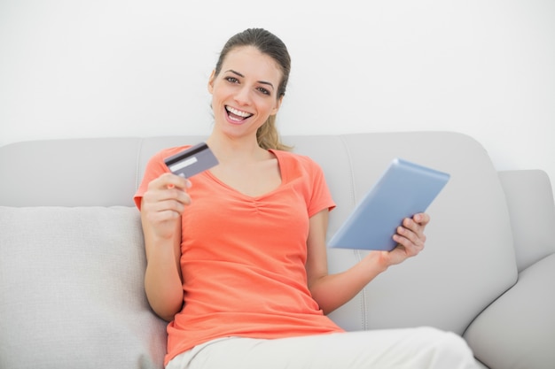 Femme amusante attrayante à la maison avec sa tablette en souriant à la caméra