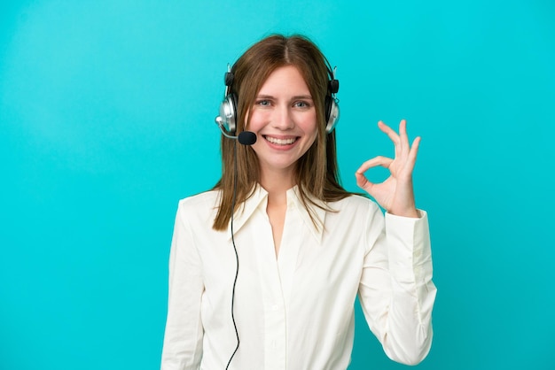 Femme anglaise de télévendeur travaillant avec un casque isolé sur fond bleu montrant un signe ok avec les doigts