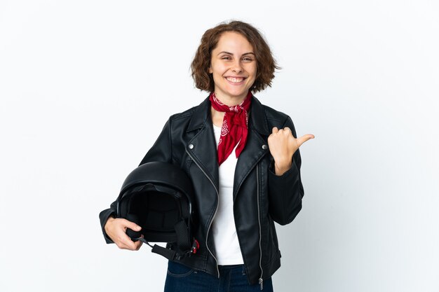 Femme anglaise tenant un casque de moto isolé sur un mur blanc pointant vers le côté pour présenter un produit