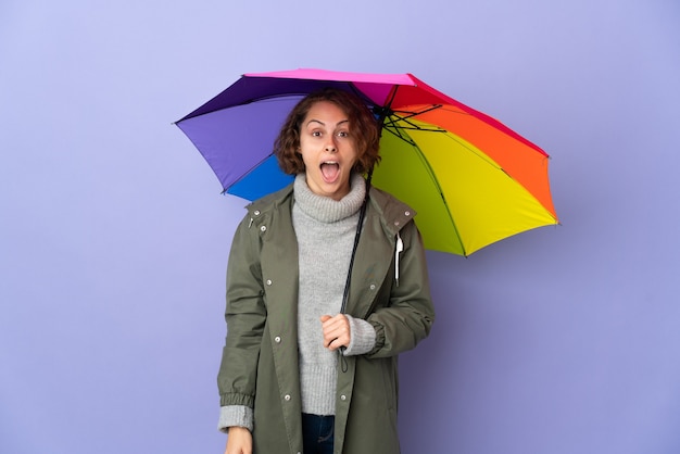 Femme anglaise tenant un parapluie isolé sur mur violet avec expression faciale surprise