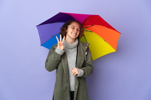 Femme Anglaise Tenant Un Parapluie Isolé Sur Mur Violet Heureux Et Compter Trois Avec Les Doigts