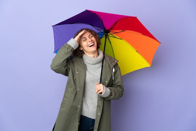 Femme anglaise tenant un parapluie isolé sur mur violet souriant beaucoup