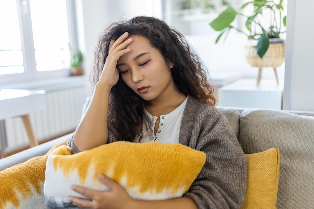 Une femme anxieuse inquiète assise sur un canapé à la maison Une asiatique frustrée et confuse ressent des problèmes malheureux dans la querelle de la vie personnelle rompre avec son petit ami et le concept de grossesse inattendue