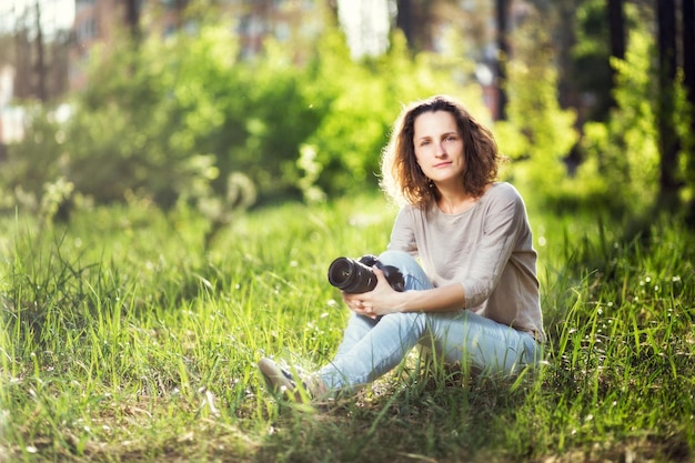 Une femme avec un appareil photo assis sur l'herbe dans le parc