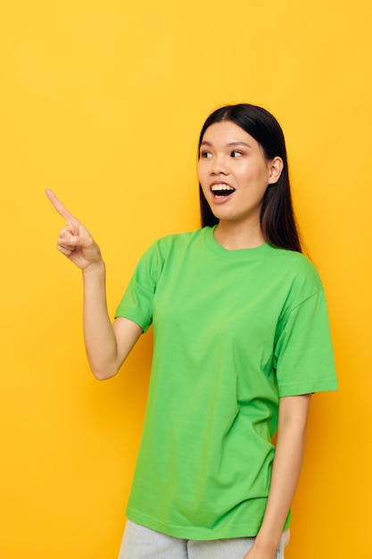 Femme d'apparence asiatique en t-shirts verts gestes avec ses mains émotions fond jaune inchangé