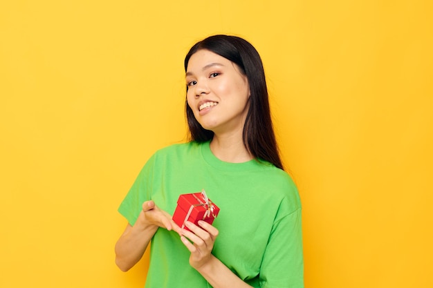 Femme d'apparence asiatique en T-shirts verts avec une petite boîte cadeau fond jaune inaltéré