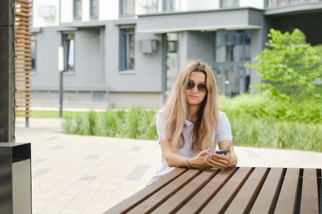 Une femme a appelé un taxi à l'aide d'une application mobile et attend sa voiture alors qu'elle est assise sur un banc