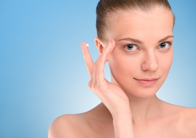 Femme appliquant la crème de levage sur le visage sur fond bleu.