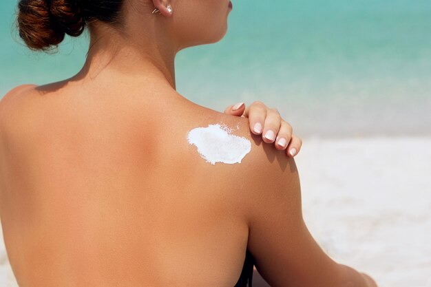 Femme appliquant de la crème solaire sur l'épaule bronzée