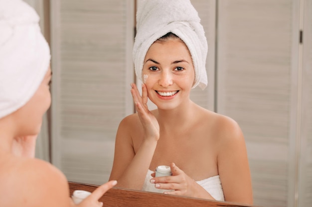 Femme appliquant de la crème sur son visage dans la salle de bain