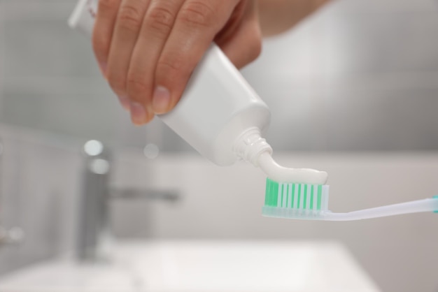 Femme appliquant du dentifrice sur la brosse dans la salle de bain agrandi