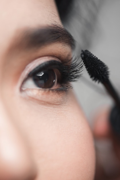 Femme appliquant du mascara à l'aide d'une baguette à cils