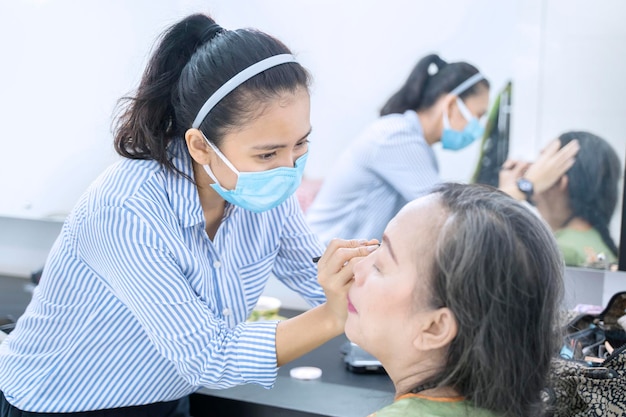 Femme appliquant un fard à paupières sur le visage de son client âgé