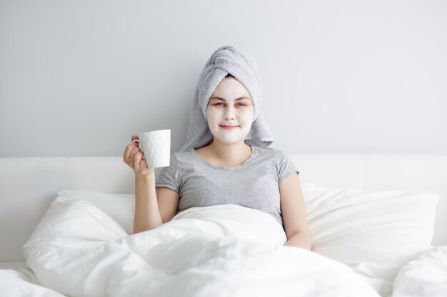 Femme appliquant un masque facial et buvant du café au lit