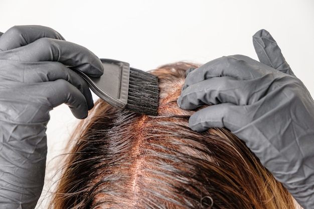 Femme appliquant une teinte de couleur sur les cheveux bruns à l'aide d'un pinceau. Teinture des racines grises des cheveux à la maison.