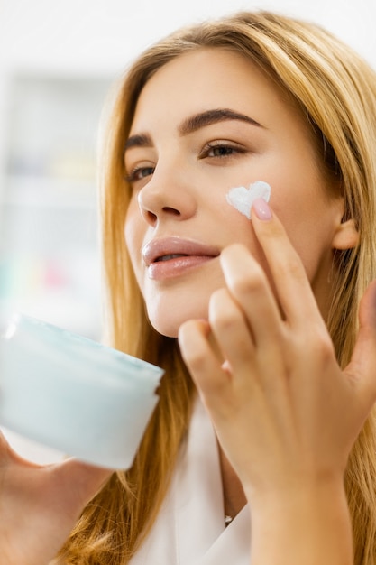 Femme applique de la crème sur son visage en forme de coeur