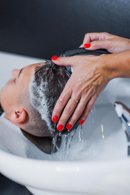Une femme applique du shampoing et masse les cheveux d'un client Le gars se lave les cheveux au salon de coiffure