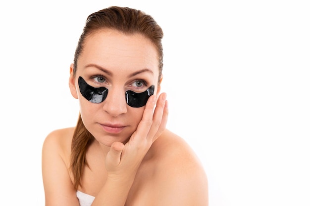 Une femme applique des taches noires cosmétiques sous ses yeux contre un mur blanc