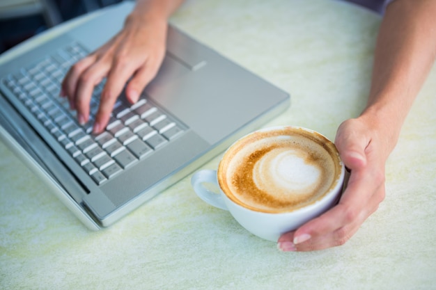 Femme appréciant un cappuccino en utilisant un ordinateur portable