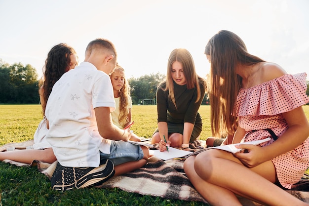 Femme apprenant à dessiner un groupe d'enfants heureux est à l'extérieur sur le terrain de sport pendant la journée