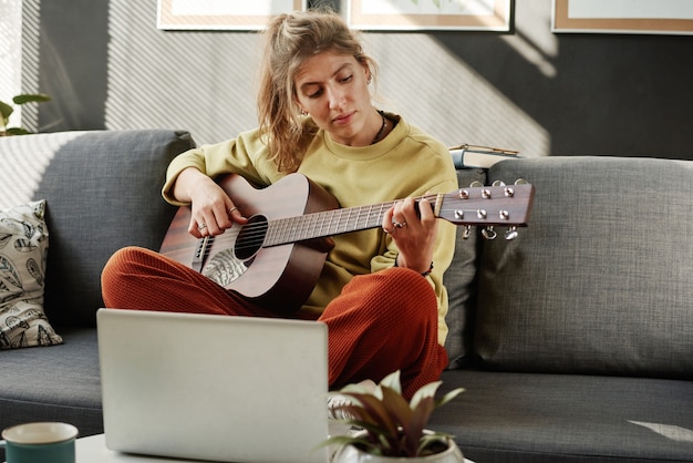 Femme apprenant à jouer de la guitare en ligne à la maison