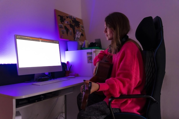 Photo femme apprenant à jouer de la guitare à la maison avec des cours en ligne sur l'ordinateur assis sur la chaise