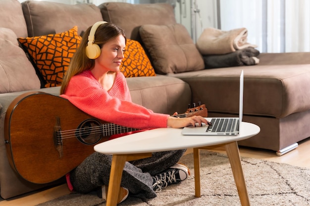 Femme apprenant à jouer de la guitare à la maison avec des cours en ligne sur ordinateur