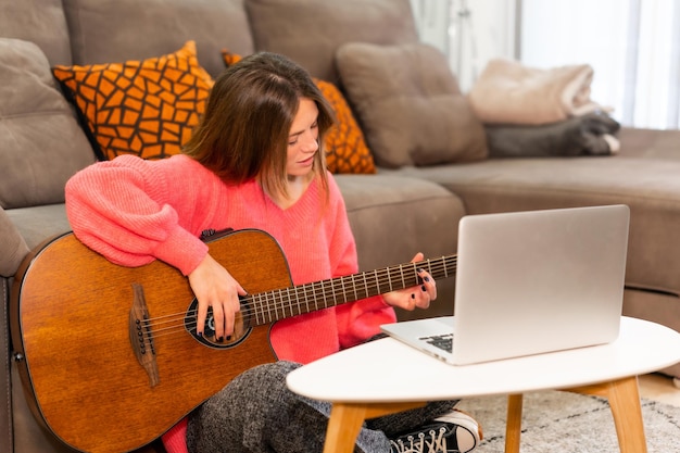 Femme apprenant à jouer de la guitare à la maison avec des tutoriels sur Internet