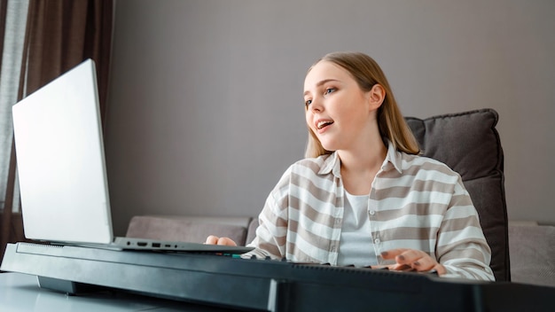 Une femme apprend la musique en chantant en jouant du piano en ligne à l'aide d'un ordinateur portable à l'intérieur de la maison