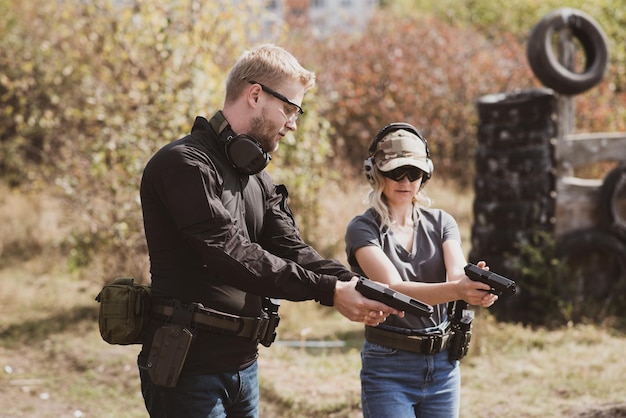 Une femme apprend à tirer avec un pistolet sur un champ de tir avec un instructeur