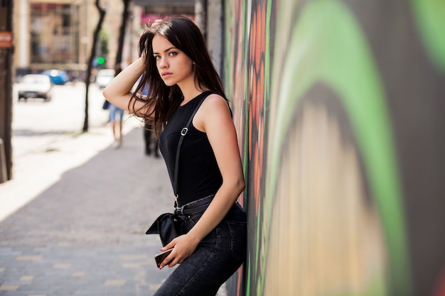 Femme appuyée contre un mur avec un téléphone dans ses mains